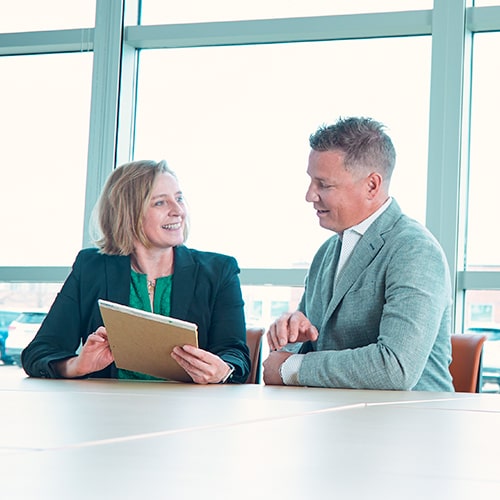 Photo of two PHB staff members, a woman on the left and a male on the right. The man is looking at a notepad that the woman is holding and the woman is looking at the man